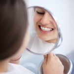 female patient examining her smile with a hand mirror